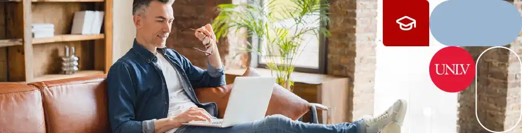 Person sitting on a brown leather couch working on a laptop with a pen in hand.